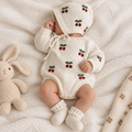 Newborn baby wearing off-white knitted romper and bonnet with cherry embroidery