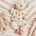 Newborn in cream knit romper and bonnet with bee motifs, matching pants