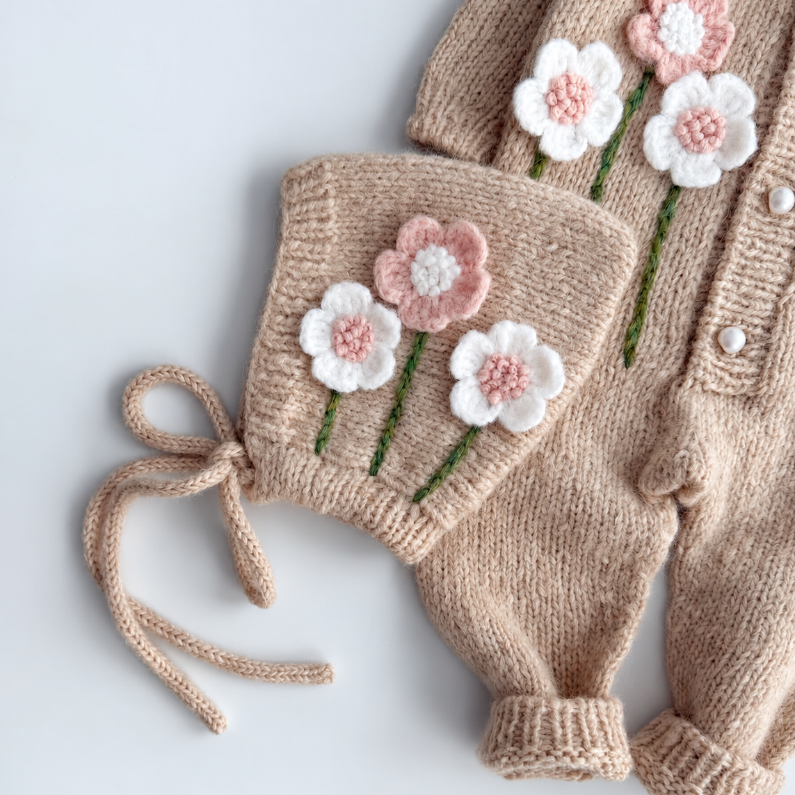 Knitted newborn booties with floral appliques, green stems, and tied bow detail
