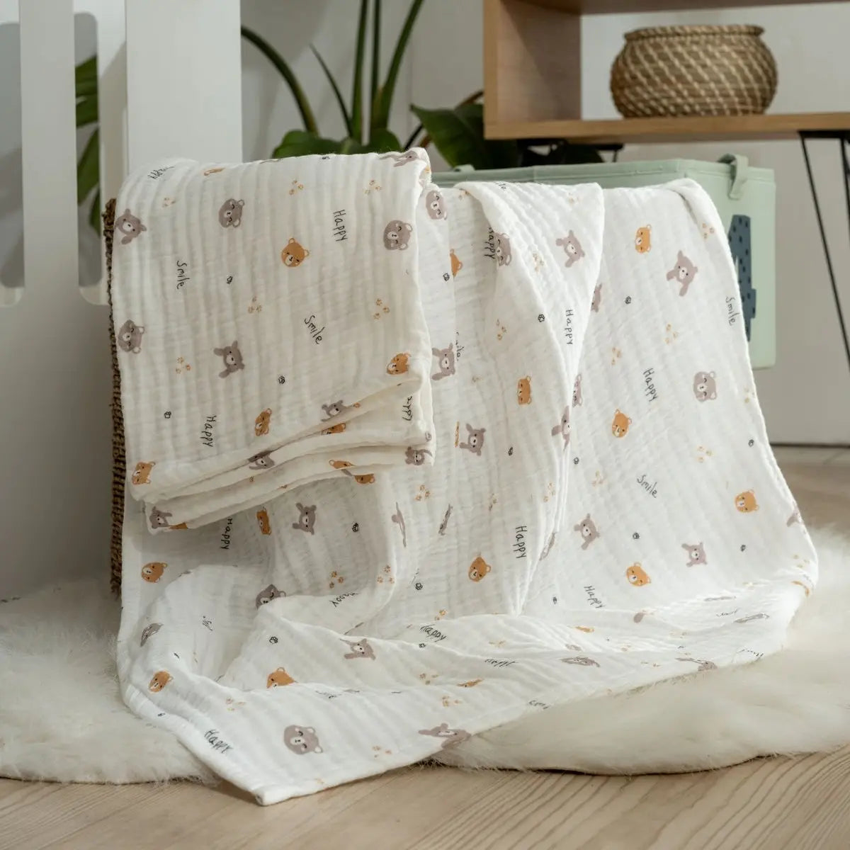White muslin baby blanket with repeating teddy and animal motifs, loosely draped on bedding